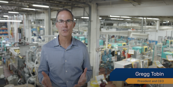 Gregg Tobin in a blue shirt is standing in a factory