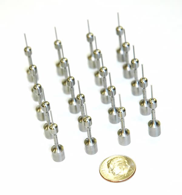 Rows of small precision-engineered metallic components with a coin for size reference